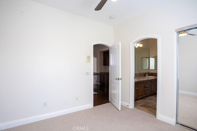 unfurnished bedroom with arched walkways, ensuite bathroom, light carpet, a sink, and baseboards