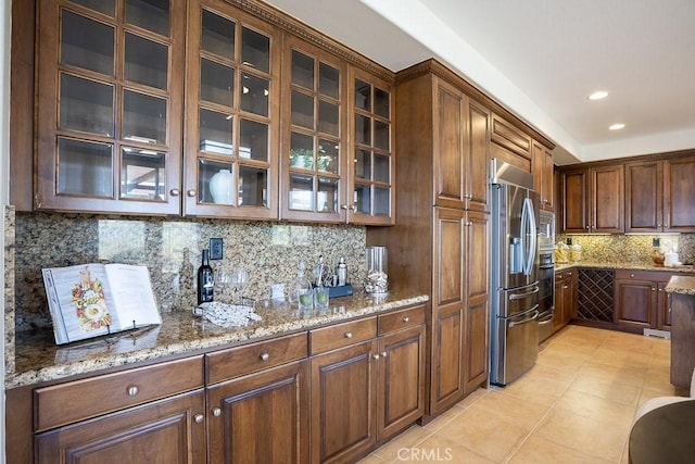 kitchen featuring light tile patterned flooring, stainless steel appliances, backsplash, light stone countertops, and glass insert cabinets