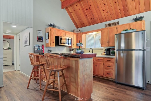 kitchen with appliances with stainless steel finishes, a breakfast bar, dark wood-style flooring, and wooden ceiling