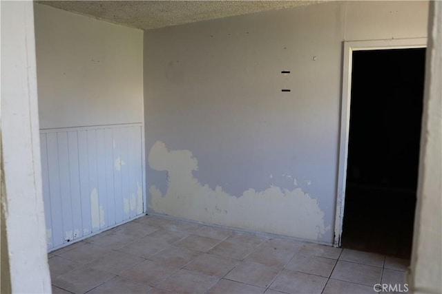 tiled empty room with a wainscoted wall and a textured ceiling