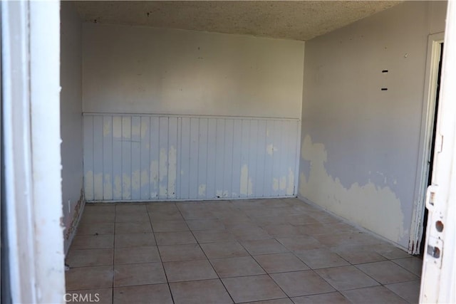 spare room with a wainscoted wall, light tile patterned floors, and a textured ceiling