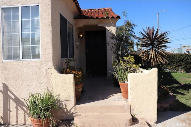 view of exterior entry with a tile roof and stucco siding