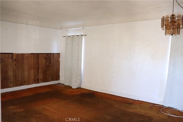 spare room featuring a notable chandelier, wood walls, and a textured ceiling