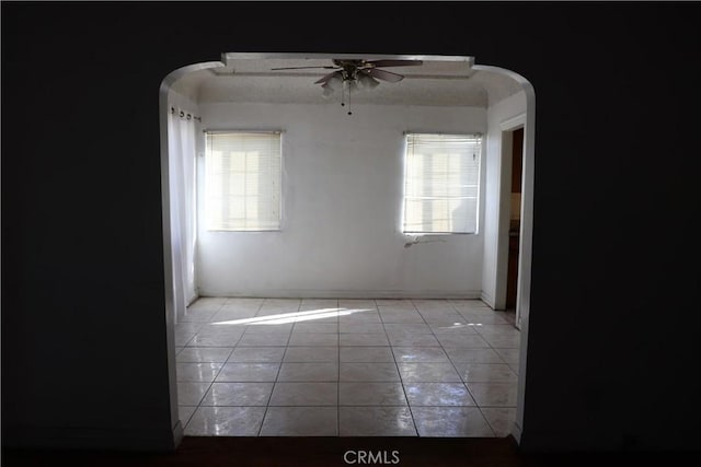 spare room with arched walkways, plenty of natural light, light tile patterned flooring, and a ceiling fan