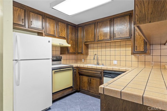 kitchen with white appliances, under cabinet range hood, tile counters, and a sink