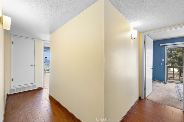 corridor featuring baseboards, a textured ceiling, visible vents, and wood finished floors