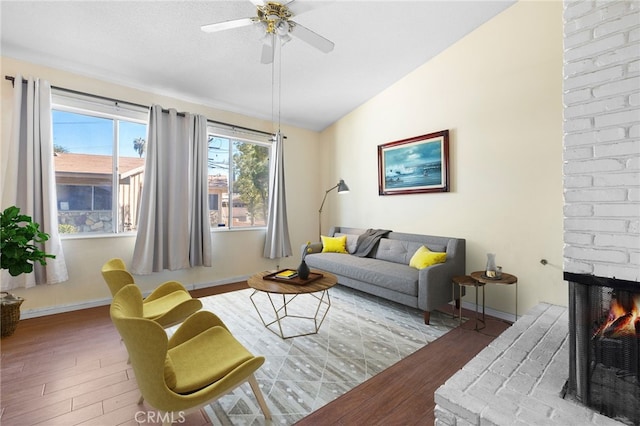 living area featuring a brick fireplace, a ceiling fan, vaulted ceiling, and wood finished floors