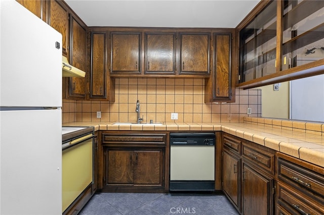 kitchen with white appliances, backsplash, dark brown cabinets, dark tile patterned floors, and a sink