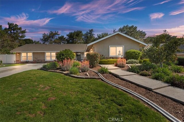 ranch-style house with a lawn, concrete driveway, stone siding, fence, and stucco siding