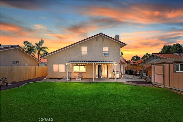 rear view of property featuring stucco siding, a lawn, an outbuilding, a patio, and a fenced backyard