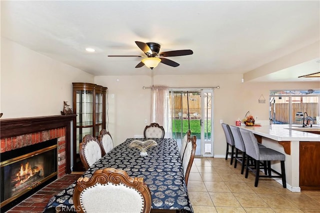 dining space featuring light tile patterned flooring, ceiling fan, a brick fireplace, and baseboards