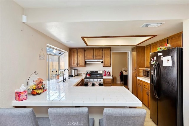 kitchen with visible vents, brown cabinets, a sink, under cabinet range hood, and stainless steel appliances