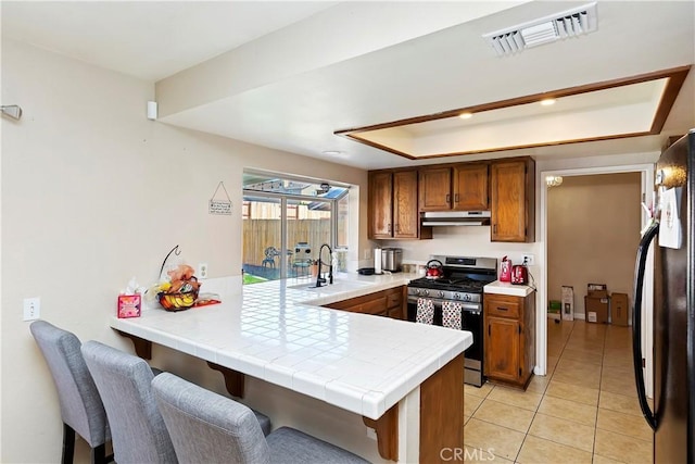 kitchen featuring stainless steel gas range oven, visible vents, under cabinet range hood, a peninsula, and a raised ceiling