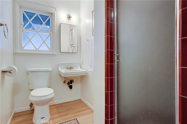 bathroom with toilet, a shower stall, baseboards, and wood finished floors