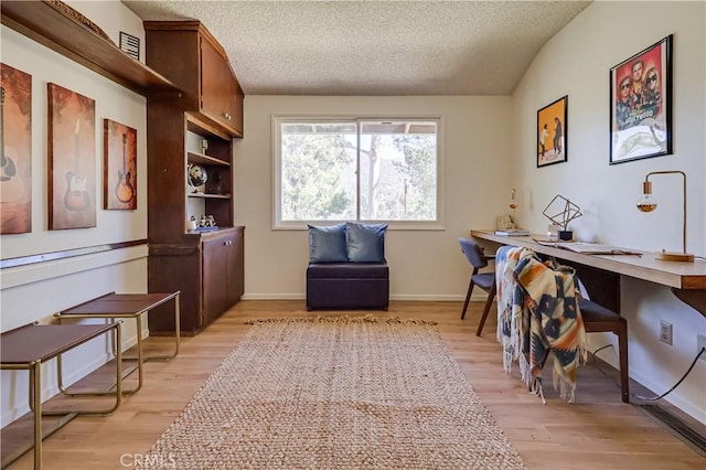 office space featuring light wood-style flooring, a textured ceiling, baseboards, and lofted ceiling