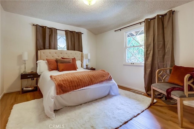 bedroom with visible vents, a textured ceiling, baseboards, and wood finished floors