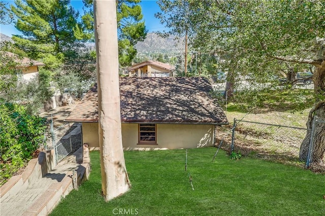 rear view of property with a shingled roof, stucco siding, a yard, and fence