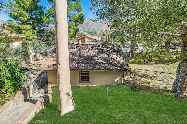 rear view of house with a shingled roof, stucco siding, fence, and a lawn