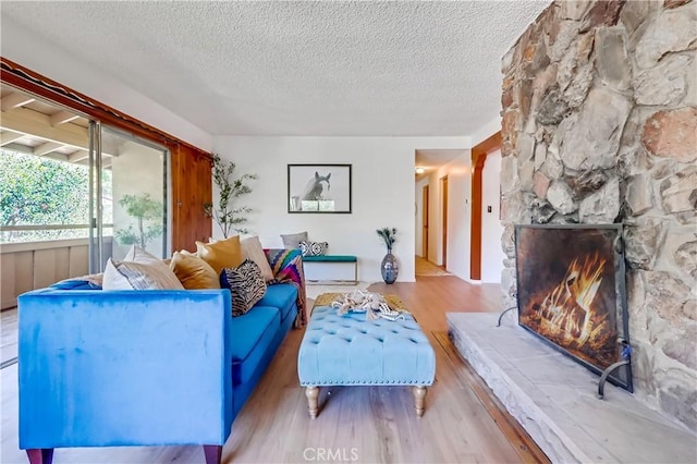 living room featuring a stone fireplace, a textured ceiling, and wood finished floors