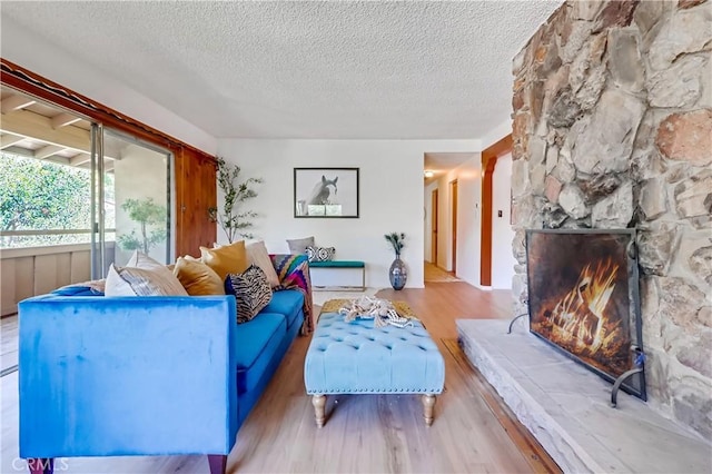 living area featuring a textured ceiling, wood finished floors, and a stone fireplace