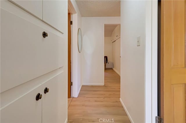 hall featuring light wood finished floors, baseboards, and a textured ceiling