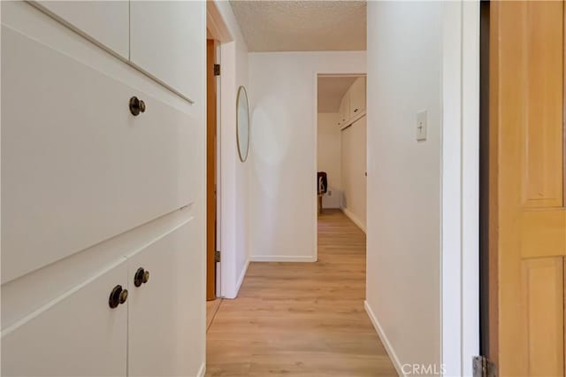 hall with light wood-style flooring, baseboards, and a textured ceiling