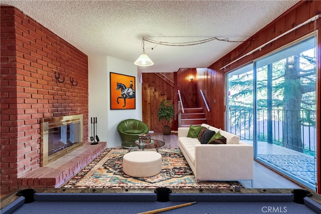 living room featuring a textured ceiling, stairway, a fireplace, and wooden walls