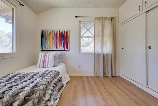 bedroom with light wood-style floors, a closet, multiple windows, and a textured ceiling