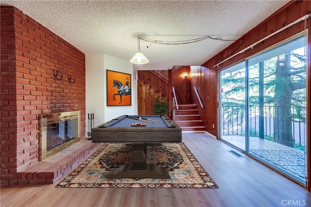 rec room with a textured ceiling, wooden walls, a fireplace, and wood finished floors