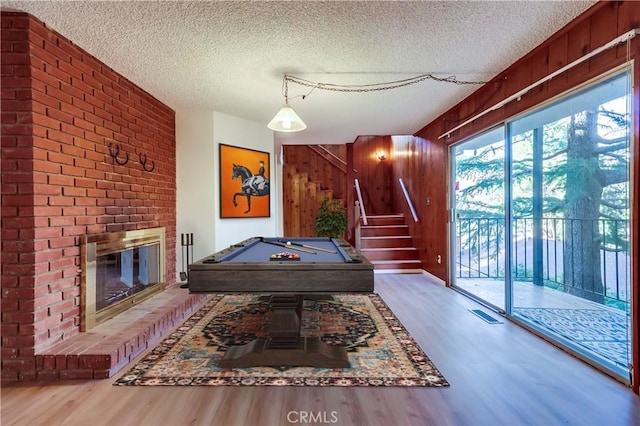 playroom featuring a textured ceiling, wood finished floors, wood walls, and a brick fireplace