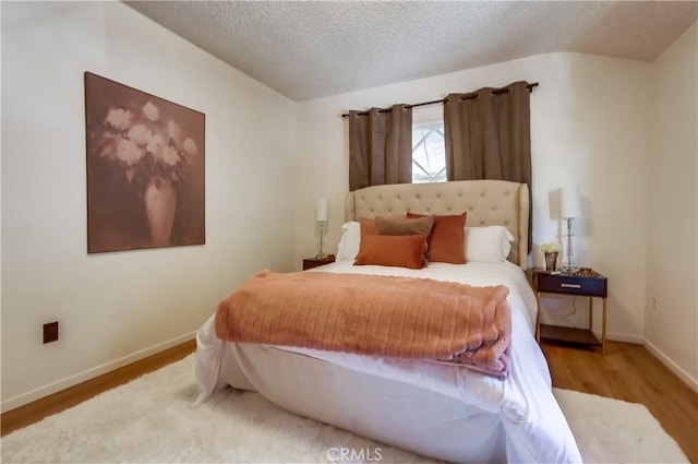 bedroom featuring a textured ceiling, baseboards, and wood finished floors