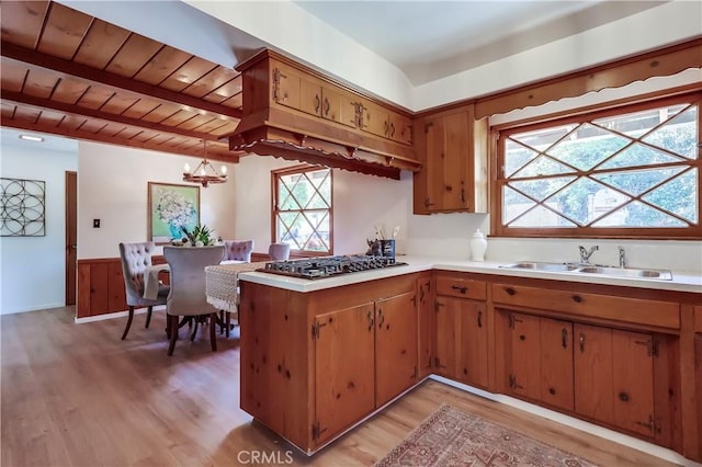 kitchen with light wood-style floors, stainless steel gas cooktop, light countertops, a sink, and a notable chandelier
