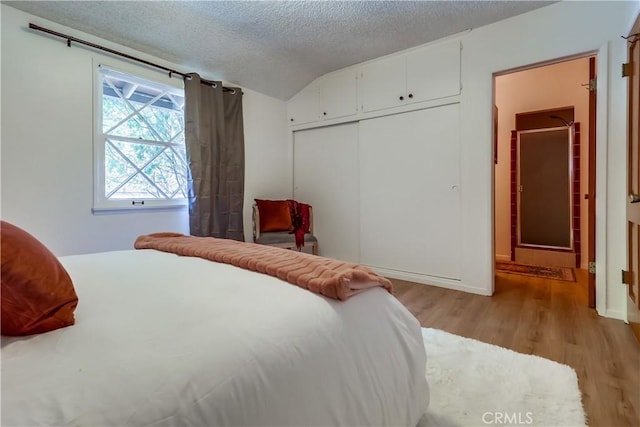 bedroom with a closet, lofted ceiling, light wood-style floors, and a textured ceiling