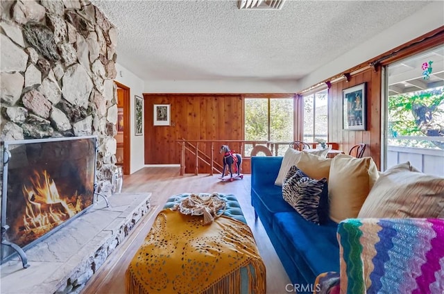 living room featuring visible vents, wood walls, a stone fireplace, a textured ceiling, and wood finished floors