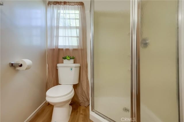 bathroom with toilet, a stall shower, wood finished floors, and baseboards