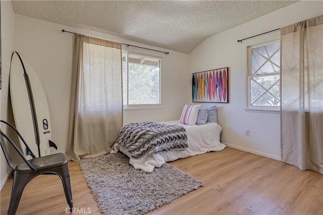 bedroom with vaulted ceiling, a textured ceiling, baseboards, and wood finished floors