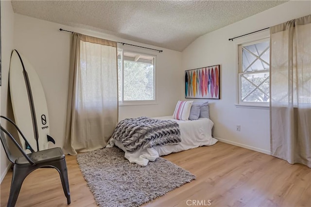 bedroom with lofted ceiling, a textured ceiling, baseboards, and wood finished floors
