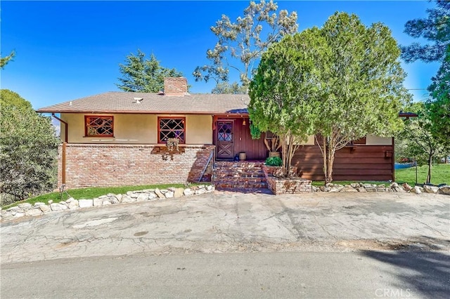 ranch-style home with brick siding, a chimney, and stucco siding