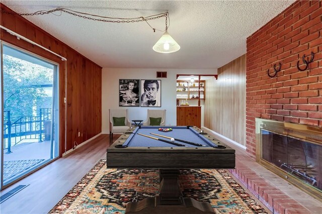 playroom with visible vents, wood finished floors, a textured ceiling, wood walls, and a fireplace