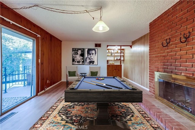 playroom featuring a fireplace, pool table, a textured ceiling, wood finished floors, and wooden walls