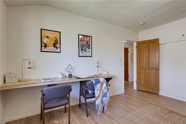 home office featuring lofted ceiling, light wood finished floors, baseboards, and a textured ceiling