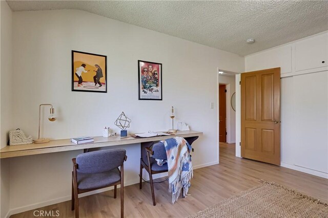 home office with light wood-type flooring, baseboards, vaulted ceiling, and a textured ceiling