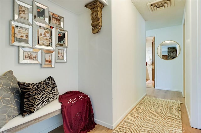 corridor featuring wood finished floors, baseboards, and visible vents