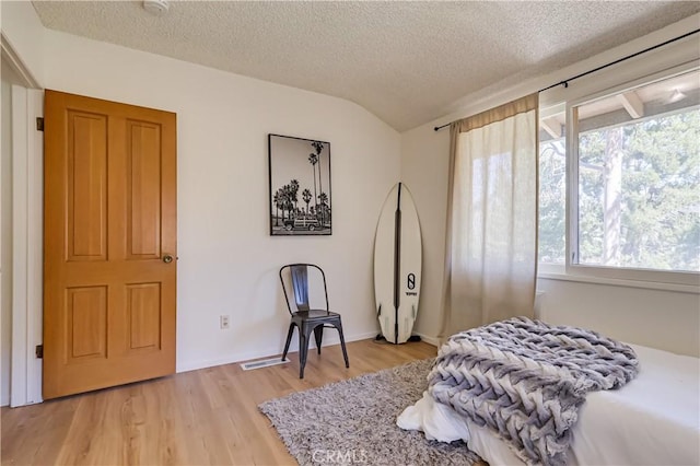 bedroom with a textured ceiling, visible vents, light wood finished floors, and vaulted ceiling