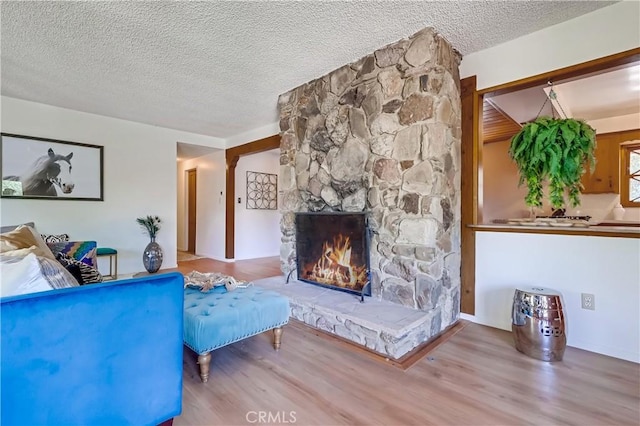 living area featuring a textured ceiling, wood finished floors, and a stone fireplace