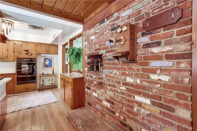 kitchen with a warming drawer, visible vents, light countertops, light wood-style flooring, and brick wall