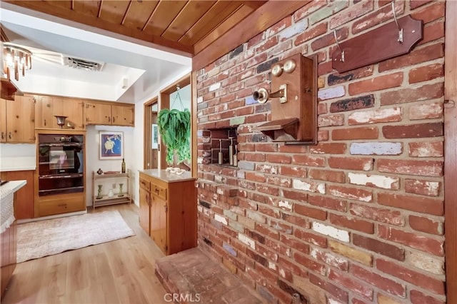 kitchen featuring visible vents, a warming drawer, light countertops, brick wall, and light wood finished floors