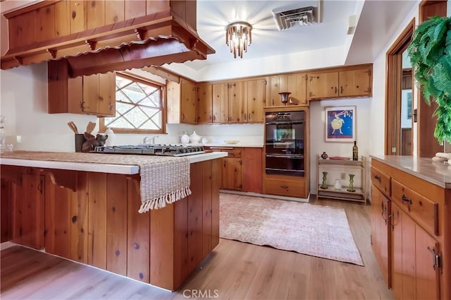 kitchen featuring a peninsula, visible vents, light wood-style floors, black oven, and light countertops