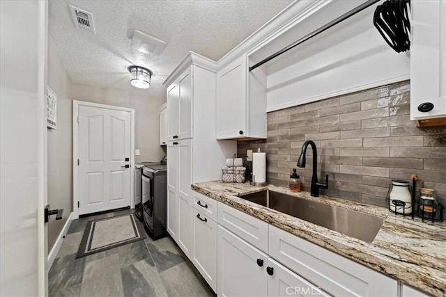 kitchen with washing machine and dryer, a sink, visible vents, white cabinets, and tasteful backsplash