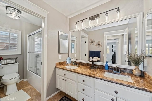 full bathroom featuring toilet, double vanity, bath / shower combo with glass door, and a sink